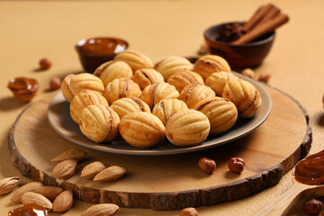 Tasty walnut shaped cookies with boiled condensed milk, almonds and hazelnuts on beige table, closeup