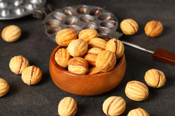 Bowl with tasty walnut shaped cookies and baking form on black grunge table, closeup