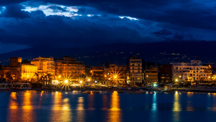 evening or night landscape of evening town coastline in golden lights and sea gulf with calm water and nice reflections with beautisul sunset sky on background