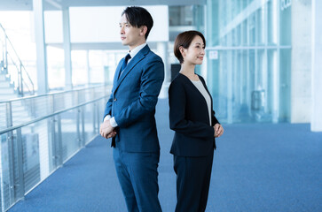 社内に立つカメラ目線のスーツを着た男女