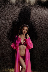 Naklejka premium A woman in a pink raincoat is standing in the rain. She is wearing a bikini and a pink robe