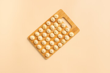 Top view of a wooden board with neatly laid out semi-cooked dumplings.