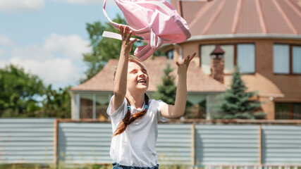 Bright emotions of child running back to school. Girl with a backpack in a jump next to school.