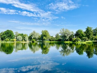 summer lake in the park, blue sky with white clouds and green trees reflection on the lake surface