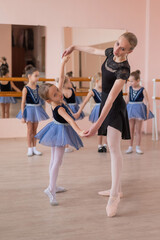 Obraz premium Children's ballet school. Caucasian woman teaching ballet to little girls. Vertical photo. 
