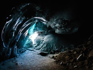 A mystical ice cave in the dark landscape emits a radiant electric blue light, resembling a...