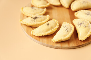 Raw samosas with poppy on a wooden round board ready for baking. Traditional Central Asian cuisine, frozen semi-finished products, copy space.