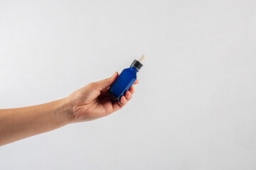 Blue glass cosmetic bottle in hand, Skin care or sunscreen cosmetic on white background.