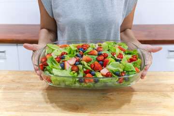 Woman holding bowl with fresh vegetable and fruit salad in the kitchen. Healthy food.