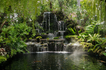 View of a beautiful artificial waterfall surrounded by lush green tropical trees.