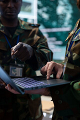 Diverse army staff collecting real time data on a laptop in control room, communicating important information for the infantry unit operations. IT engineers working in command center. Close up.