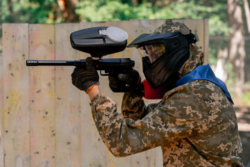 in the wild near tree structures player in a pintball uniform holds a pistol with a red balloon...