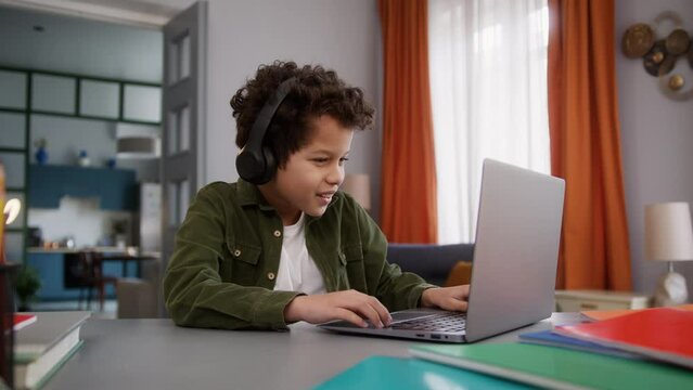 African American ethnic little boy gamer child kid son male user play online internet game laptop video gaming computer playing at home in wireless headphones pc win success achieve celebrate victory