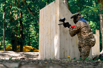 Fototapeta premium in the wild near tree structures player in a pintball uniform holds a pistol with a red balloon team game camouflage clothing