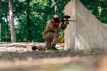 in the wild near tree structures player in a pintball uniform holds a pistol with a red balloon...