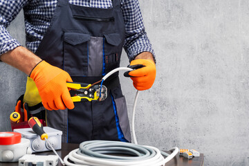 electrician worker striping the insulation of wires. electrician working against concrete wall.