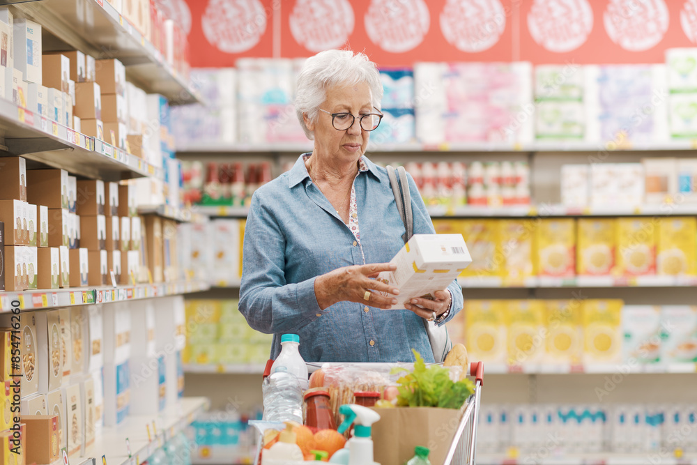 Wall mural senior woman reading information on a product package at the supermarket