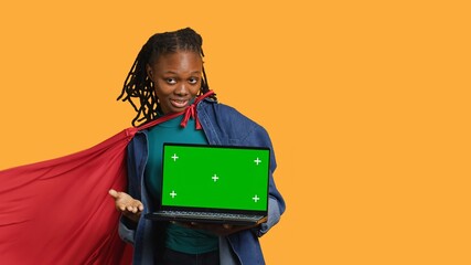 Portrait of BIPOC woman portraying superhero with cape presenting isolated screen laptop, studio...