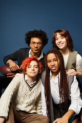 A diverse group of young friends, including a nonbinary person, sit closely together in stylish attire on a dark blue background.