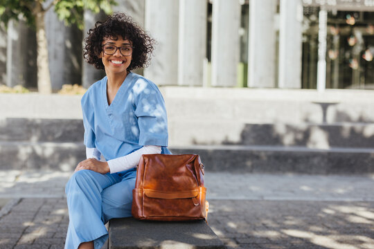 Happy female student sitting on campus in medical scrubs, ready to start her clinical rotation