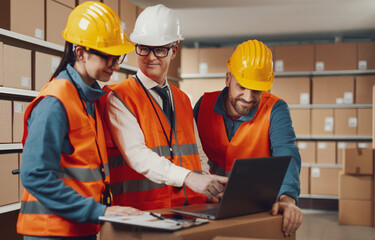 Warehouse employees working together and checking orders on a laptop