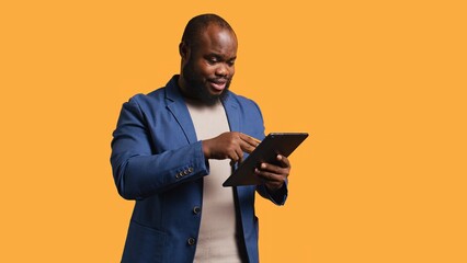 Irked man upset after lacking money while trying to buy stuff online. Grumpy person looking at debit card after getting transaction rejected on tablet, doing facepalm, studio background, camera B