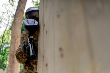 close up in the wild near tree structures player in a pintball uniform holds a pistol with a red balloon team game camouflage clothing