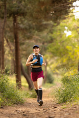 A woman is running through a forest with a backpack on her back. She is wearing a red shirt and black shorts