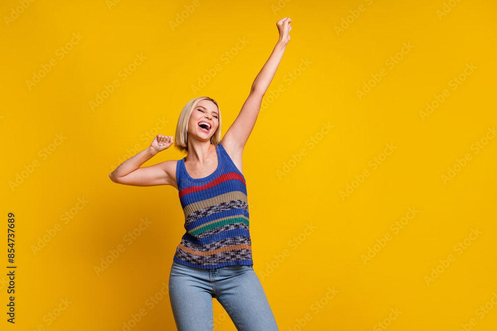 Poster Photo of young blonde bob hair lady in striped casual singlet dancing raised arms up at crazy party isolated on yellow color background