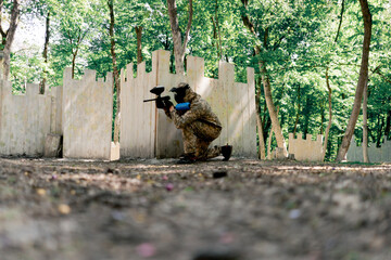 in the wild near tree structures player in a pintball uniform holds a pistol with a blue balloon...