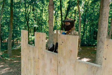 in the wild near tree structures player in a pintball uniform holds a pistol with a blue balloon...