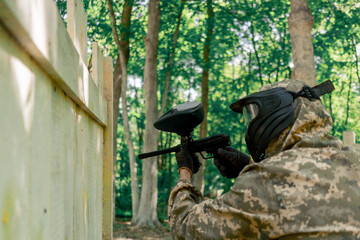 in the wild near tree structures player in a pintball uniform holds a pistol with a blue balloon...