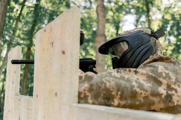 close up in the wild near tree structures player in a pintball uniform holds a pistol with a blue...