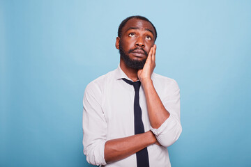 Portrait of african american employee in a white shirt daydreaming and looking up, palm to his...
