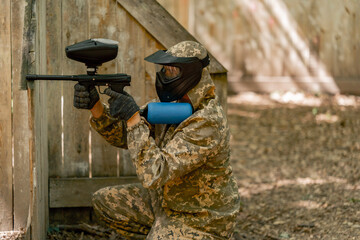 in the wild near tree structures player in a pintball uniform holds a pistol with a blue balloon...