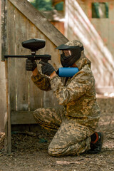 Obraz premium in the wild near tree structures player in a pintball uniform holds a pistol with a blue balloon team game camouflage clothing