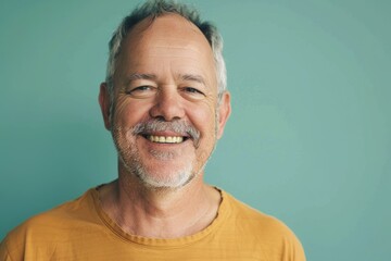 Obraz premium Portrait of a content man in his 50s smiling at the camera while standing against soft teal background