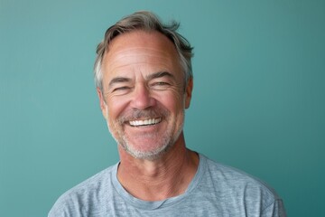 Fototapeta premium Portrait of a content caucasian man in his 50s smiling at the camera over soft teal background