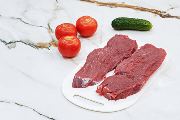 Raw beef steak with tomatoes and cucumber on natural marble table