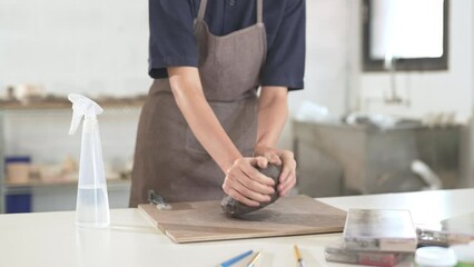 4K Asian woman sculptor artist kneads soft clay on the table at ceramic studio. Professional craftsman molding raw clay create pottery shapes at workshop. Small business handicraft product concept.