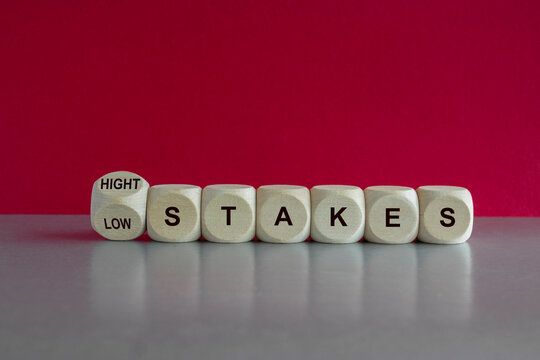 High or low stakes symbol. Concept words High stakes and Low stakes on wooden cubes. Beautiful gray table pink background. Business high or low stakes concept.