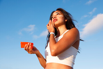 young woman applying sunscreen on her face, skincare in front of blue sky. Product photography...