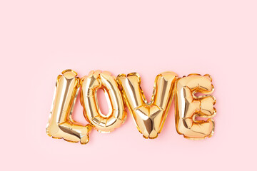 Word Love. Golden foil inflatable balloons on a pink background.