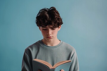 Teenage boy reading book on light blue background, Teenage Boy Immersed in Reading Against a Light Blue Background, Young Book Lover, Teen Reading Against a Serene Blue Backdrop