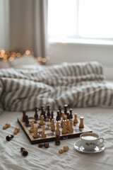 Chess board with cup of coffee on bed. Strategy thinking. Morning ideas concept. Pastel shades. Top view of unmade bedding sheets and blanket