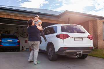 Mum in her thirties with happy five year old son outside home with family car swinging boy around