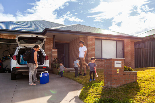 Mum packing family car before sports training with kids playing with hockey sticks on front lawn - Powered by Adobe