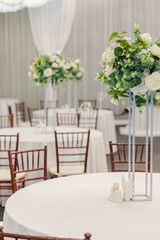 Decorated interior for festive event. Fancy table set for dinner with white flower composition in restaurant, luxury interior background. Wedding elegant banquet decoration arranged by catering