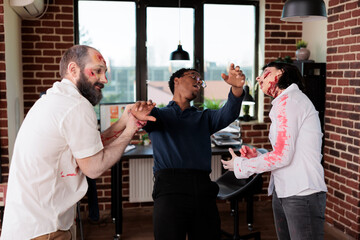 Employees wearing zombie costumes messing around with BIPOC manager in office. Team leader and...