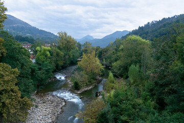 View of the Sella River passing through Cangas de Onis surrounded by dense vegetation and a beautiful mountain landscape. Cangas de Onis - Asturias